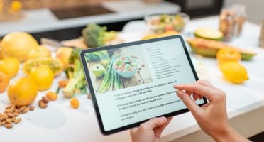 Woman looking on the digital recipe, using touchscreen tablet while cooking healthy meal on the kitchen at home, close-up view on the screen