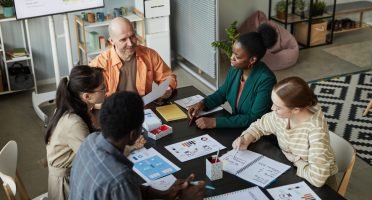 High angle view of creative business team at meeting table discussing project with smiling bald man listening to colleagues